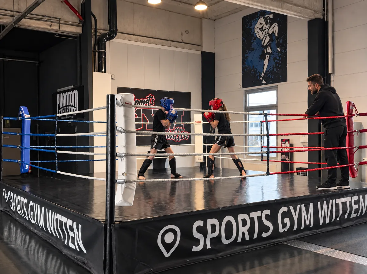 Zwei Kinder beim kontrollierten Sparring im Ring des Sports Gym Witten, mit Kopfschutz, Handschuhen und Schienbeinschonern, ein Trainer beobachtet von außen